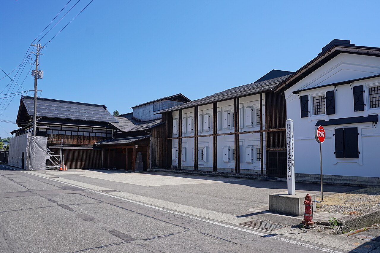 秋田県湯沢市前森の両関酒造の建物の並び。黒い板壁の木造の建物と、白い漆喰の土蔵が道に沿って続き、手前に「両関酒造本館ほか4棟」と書かれた国の登録有形文化財の標柱が立つ