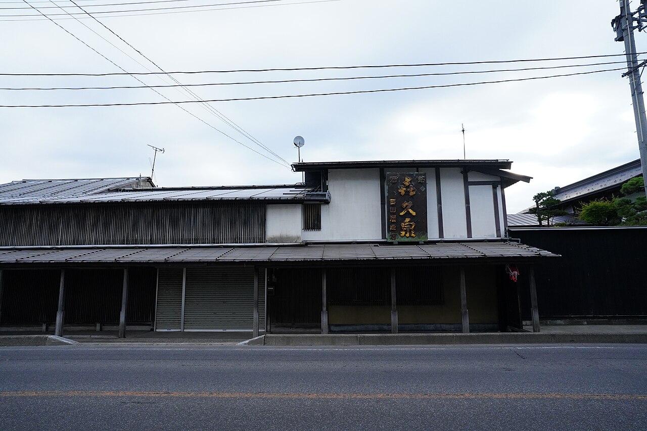 曇りの日の西田酒造店の建物。道路に面して長い庇とシャッターが並び、2階の白い壁に「喜久泉」「西田酒造店」と書かれた縦長の看板が掲げられている
