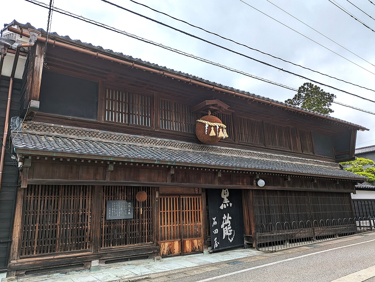 永平寺町松岡にある黒龍酒造の店舗兼主屋。二階建ての木造の町家で、格子の窓が並び、軒下に大きな杉玉が下がる。入口には「黒龍 石田屋」と書かれた黒い暖簾がかかる
