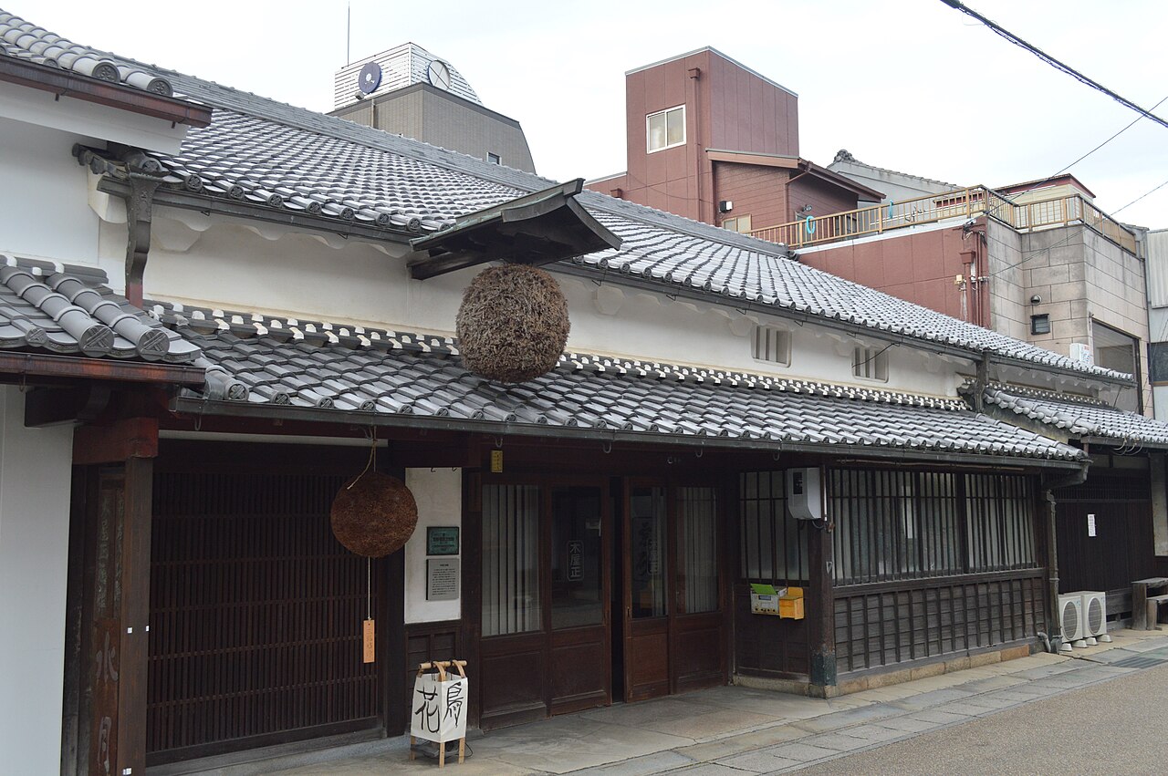 三重県名張市本町にある木屋正酒造の建物。瓦屋根と白壁の町家で、軒先に杉の葉を丸めた杉玉が2つ下がり、格子の戸が並んでいます