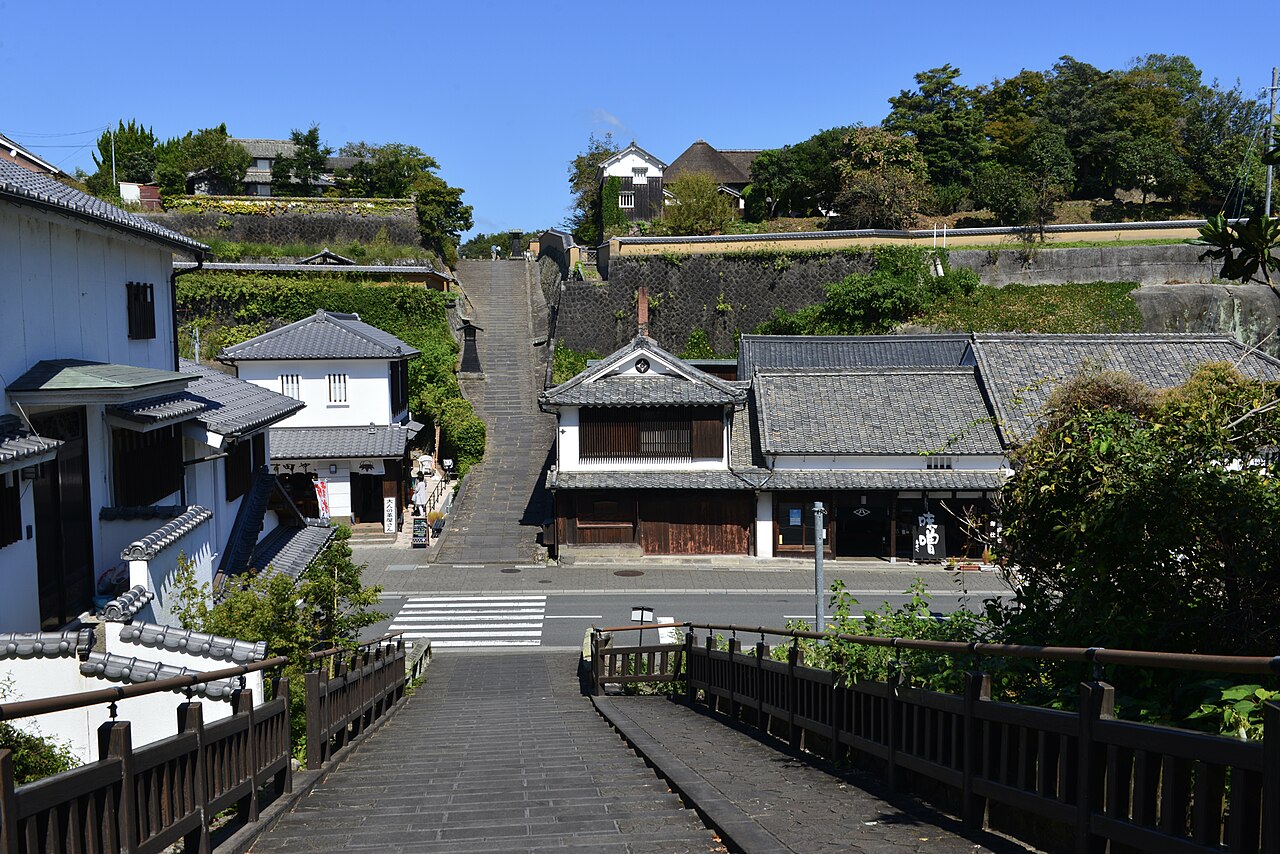 杵築の城下町。手前の塩屋の坂から、谷の通りと白壁の町家を越えて、向かいの高台へ上る酢屋の坂の石段が見える。晴れた空の下