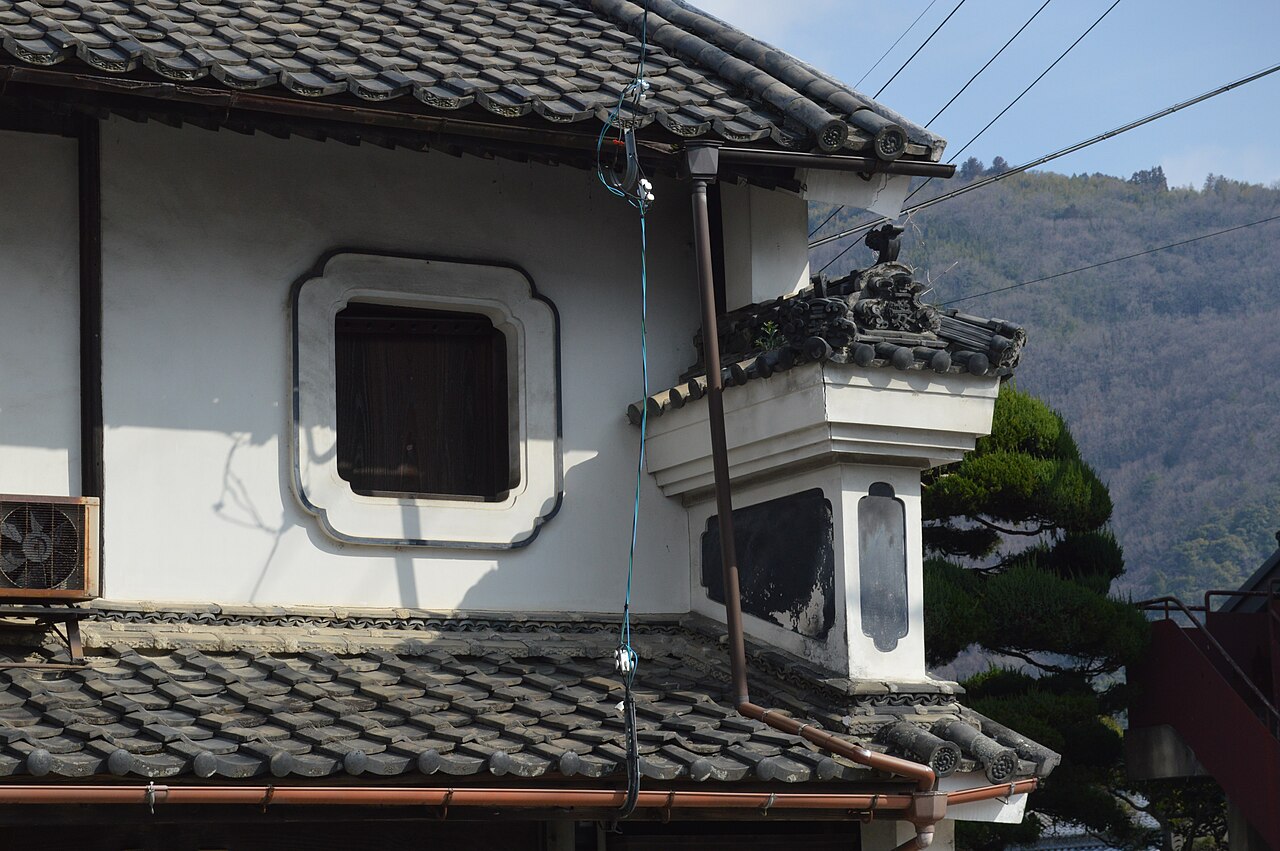 三芳菊酒造の白壁の建物に付いた、瓦屋根のうだつと虫籠窓。背後に山が見える
