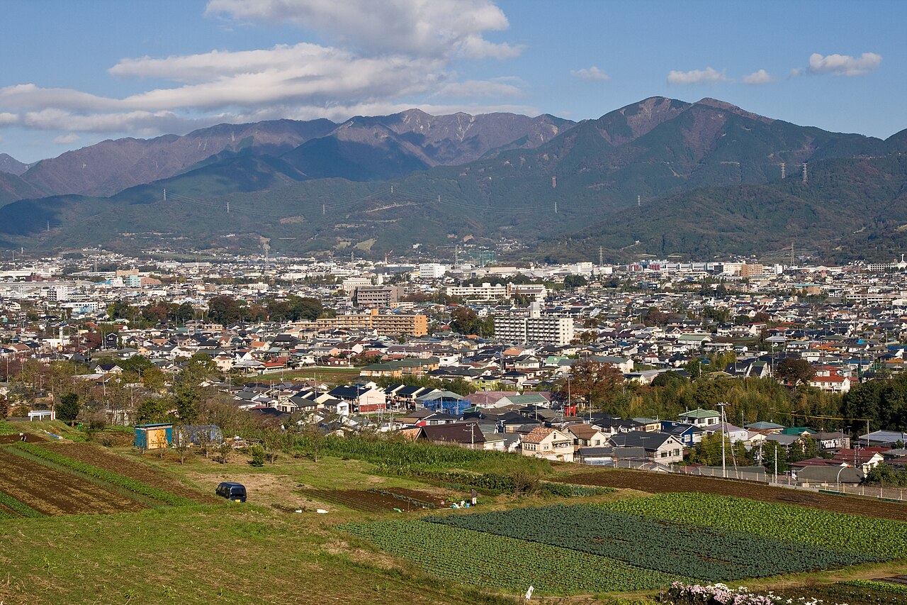 秦野市の渋沢丘陵から見た秦野盆地と丹沢の山々。手前に畑、その先に盆地の市街地が広がり、奥に丹沢の山並みが連なる