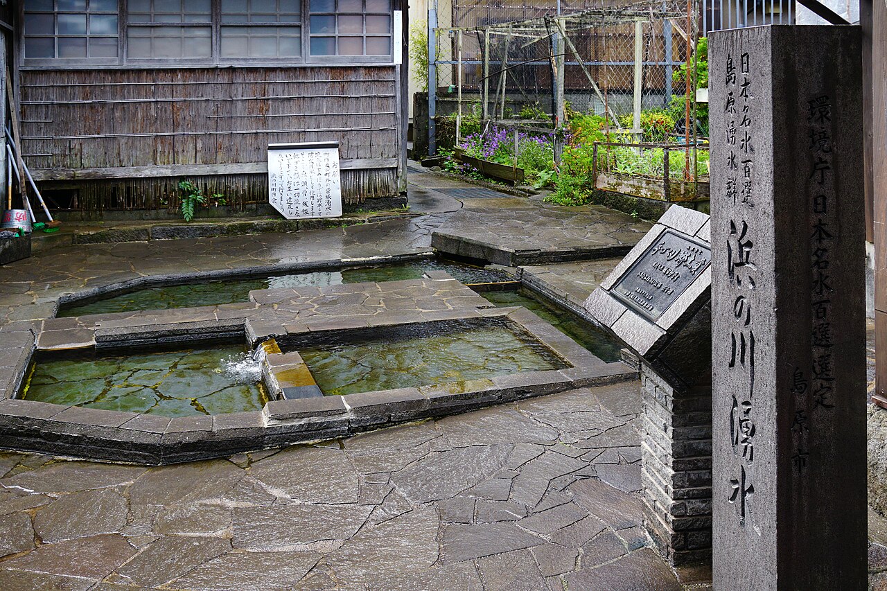 島原市の浜の川湧水。石畳の中に石で囲った水場が並び、澄んだ湧き水がたまっている。手前に「日本名水百選 島原湧水群 浜の川湧水」と刻まれた石柱が立つ