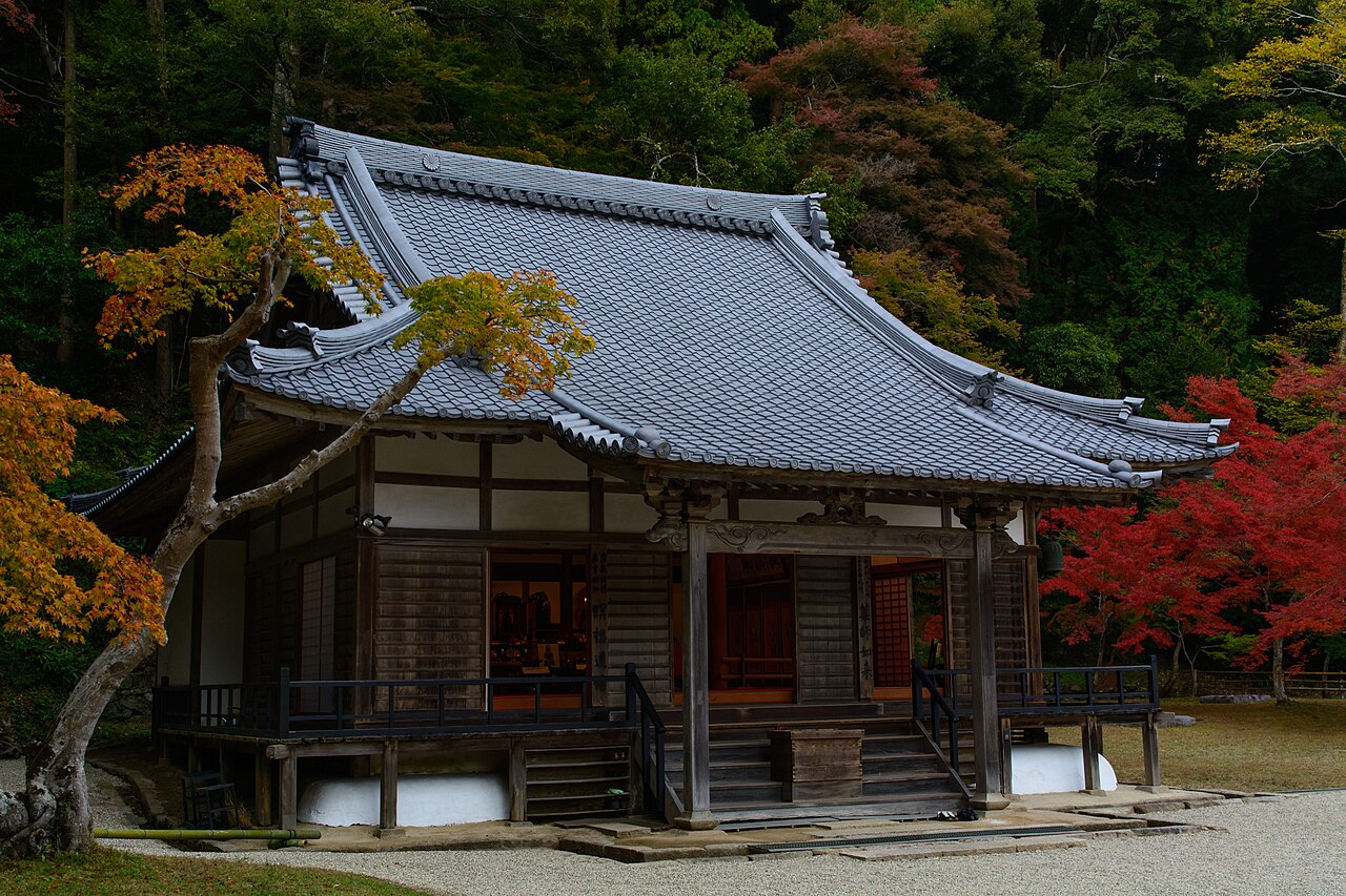 奈良市の正暦寺の本堂。瓦屋根の木造の堂の前に紅葉した木が枝を伸ばし、背後の山は赤や黄に色づいた木々と常緑の木々に覆われている