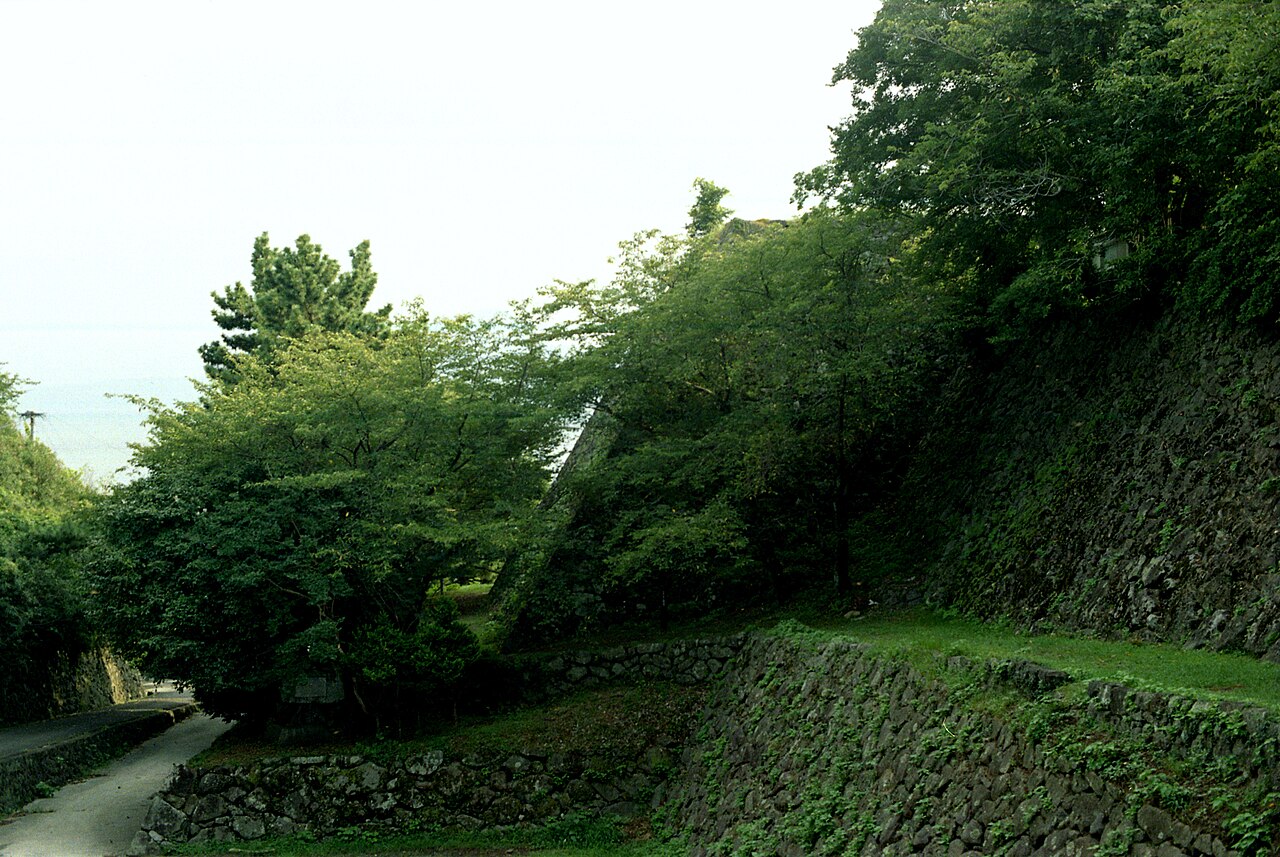 暘谷城の跡に残る石垣。苔むした石垣が段になって続き、木々の茂る斜面の奥に、白くかすむ空と海が見える