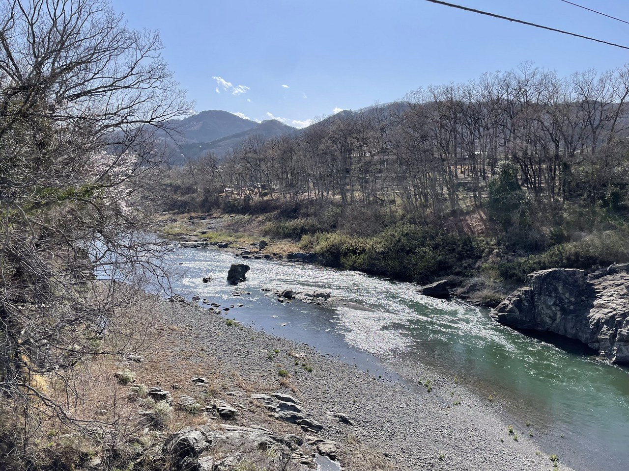 長瀞町の高砂橋から見た荒川。石の河原の向こうを澄んだ緑色の水が流れ、右岸には岩が突き出し、奥に芽吹き前の木々と山並みが続く