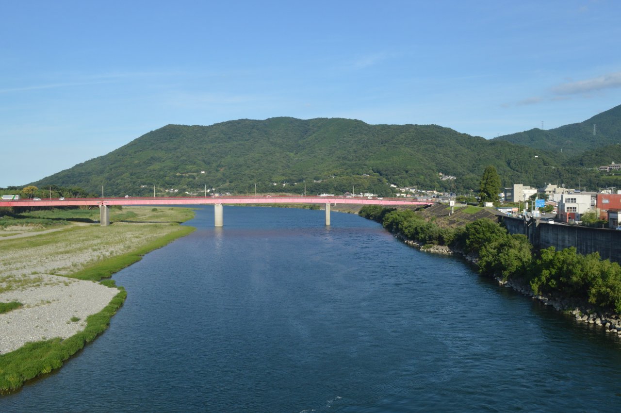 美馬市を流れる吉野川。青い川面の先に赤い穴吹橋が架かり、その奥に緑の山が連なる