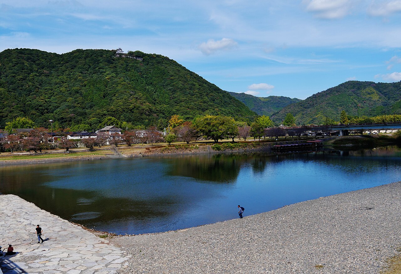 岩国市を流れる錦川。手前に石畳と砂利の河原が広がり、川の向こうの緑の山の頂に岩国城の天守が建つ。川面に山が映る